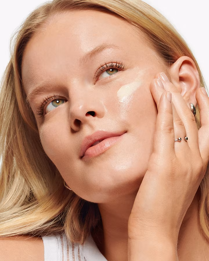 Close up of blonde model applying Clinique Pop Lip + Cheek Oil in Black Honey to cheeks